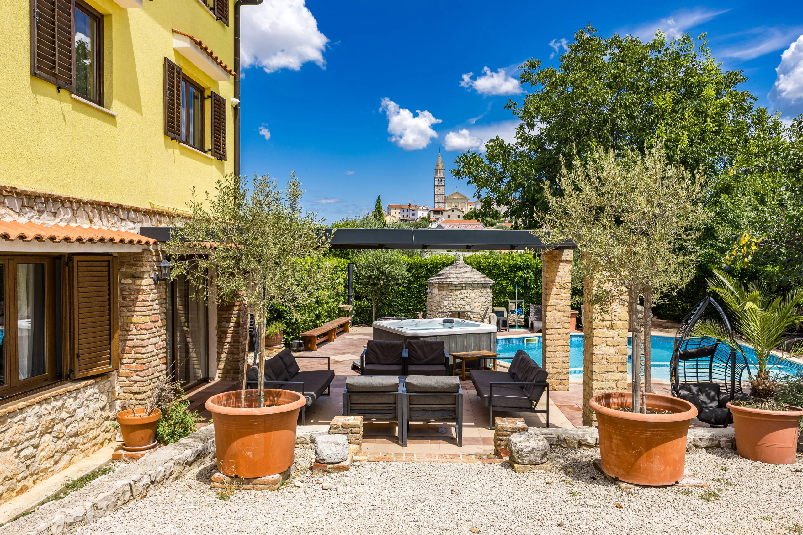 Steinterrasse unter der Pergola mit Außenlounge und Whirlpool dahinter
