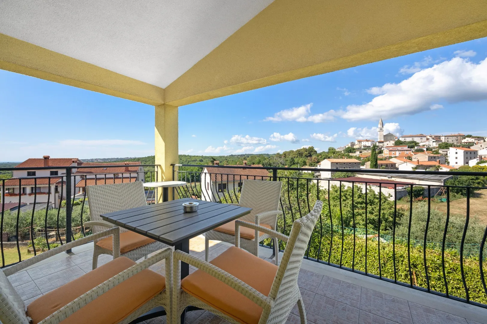 Ein Balkontisch mit vier Stühlen über den Dächern, dahinter die Dorfkirche