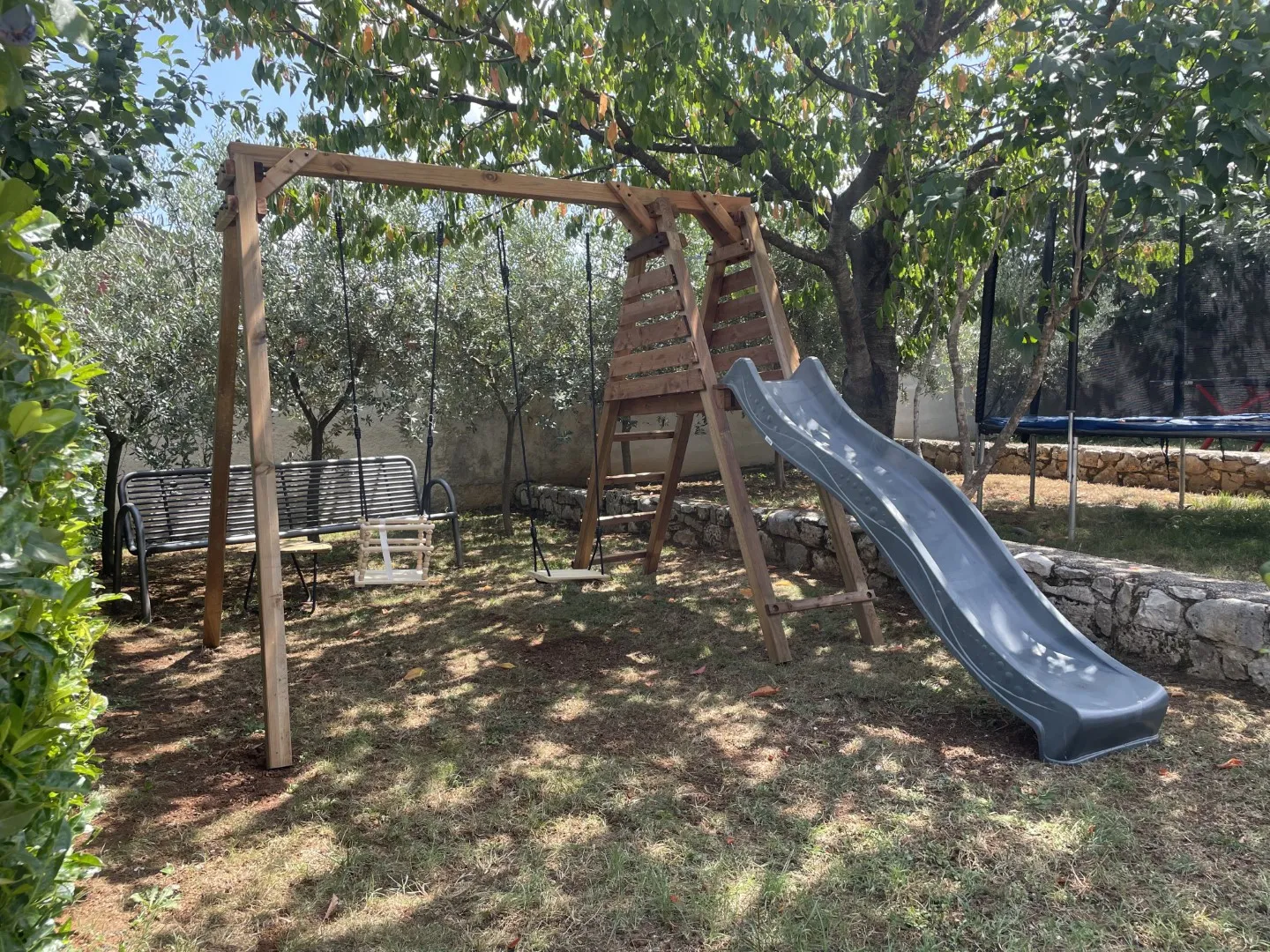 Der Kinderspielplatz mit Rutsche und Schaukel unter den Gartenbäumen