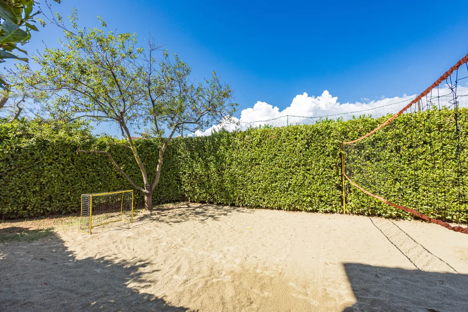 Der heckengesäumte Sandplatz im Garten, bereit für Ballspiele in der Gruppe