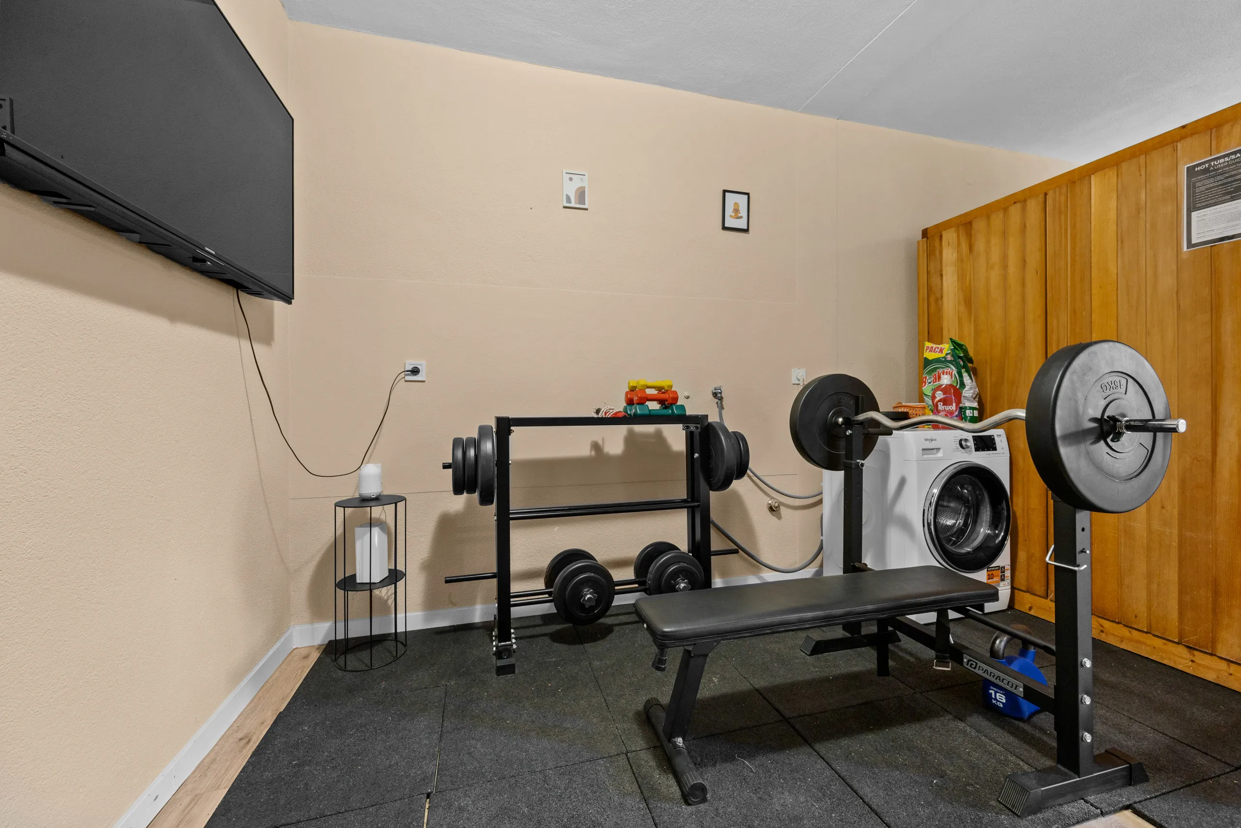 Hantelbank, Langhantel und Kurzhantelständer auf dem Mattenboden des Fitnessraums