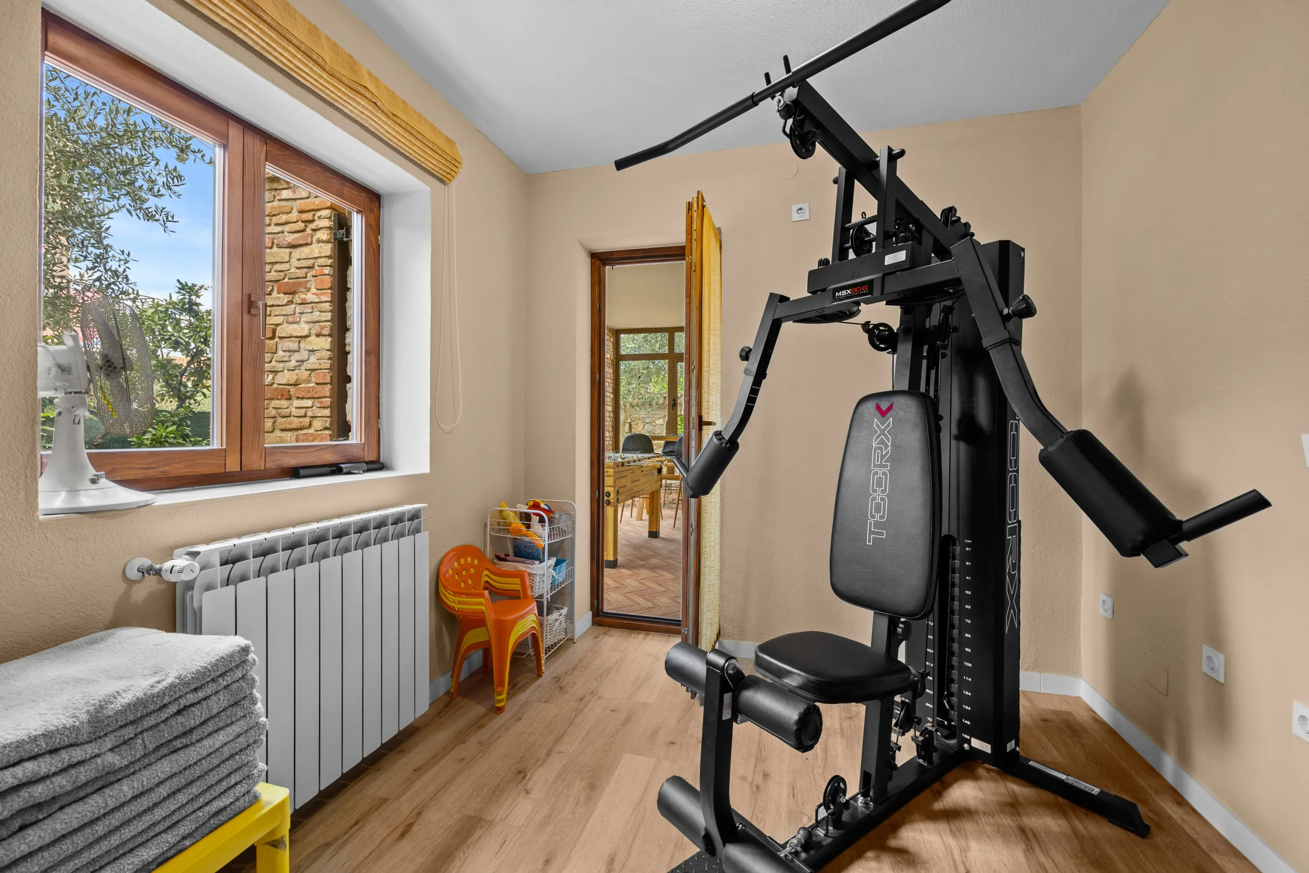 Die Kraftstation im Fitnessraum, im Fenster ein Olivenbaum