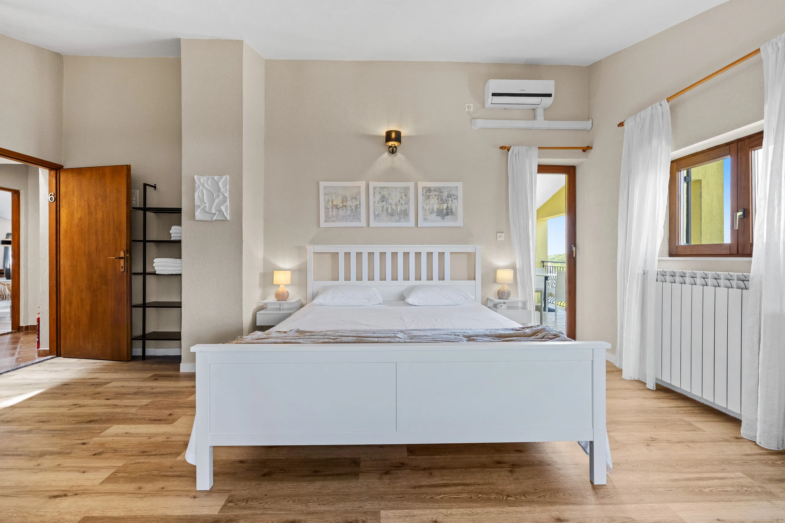 Ein Doppelzimmer mit weißem Bettgestell und Glastür zum Balkon